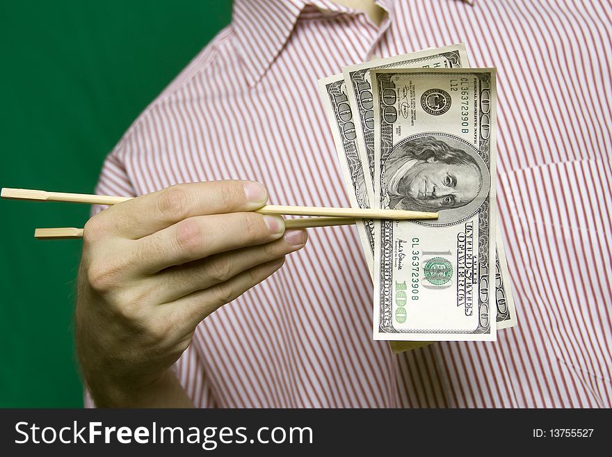 A young man in a striped shirt on a green background holding wooden chopsticks from Sushi hundred dollar bills. A young man in a striped shirt on a green background holding wooden chopsticks from Sushi hundred dollar bills