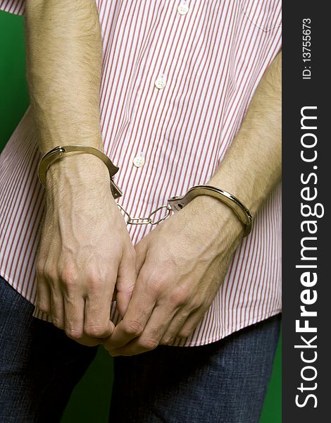 Caucasian man in a striped shirt on a green background hands handcuffed. Caucasian man in a striped shirt on a green background hands handcuffed