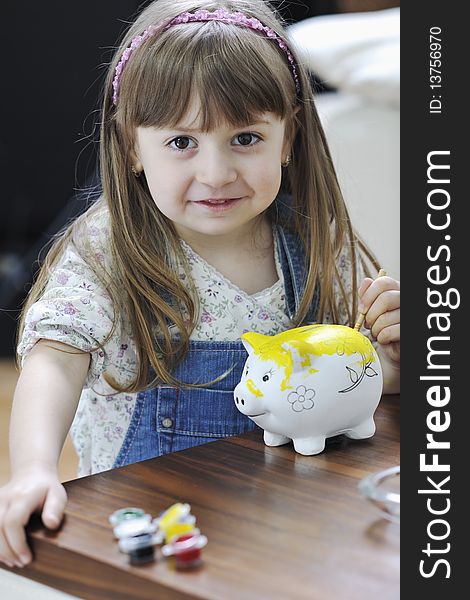 Happy young girl  portrait at home while painting piggy bank and representing banking and finance concept. Happy young girl  portrait at home while painting piggy bank and representing banking and finance concept