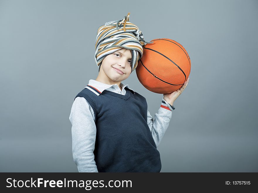 Young and funny caucasian tenager boy holding basketball ball near head and having fun with scarf around head standing isolated on gray background. Young and funny caucasian tenager boy holding basketball ball near head and having fun with scarf around head standing isolated on gray background