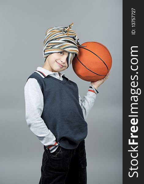 Young and funny caucasian tenager boy holding basketball ball near head and having fun with scarf around head standing isolated on gray background. Young and funny caucasian tenager boy holding basketball ball near head and having fun with scarf around head standing isolated on gray background