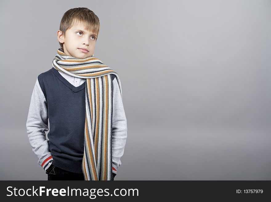 Young and patient caucasian teenager elegant boy standing with hands in pockets and wearing coloful long scarf with calm look standing isolated over gray background with copyspace. Young and patient caucasian teenager elegant boy standing with hands in pockets and wearing coloful long scarf with calm look standing isolated over gray background with copyspace