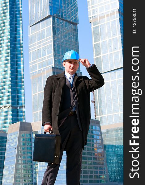 Engineer with blue hard hat holding briefcase on skyscrapers background