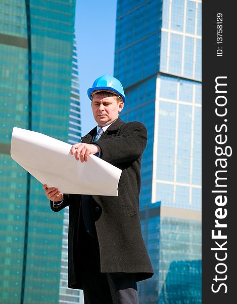Engineer with blue hard hat holding drawing on skyscrapers background