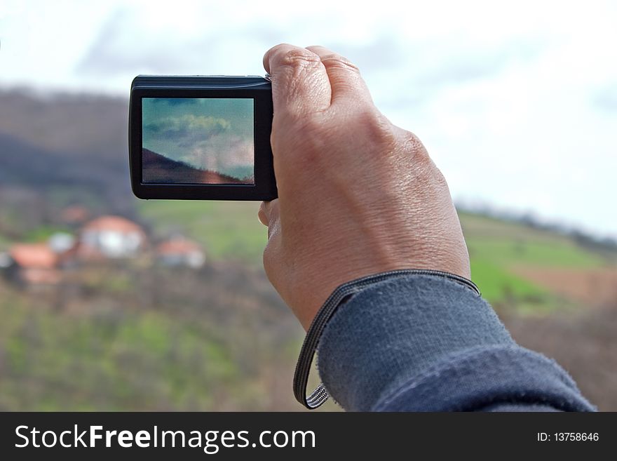 Digital camera in a hand taking photo of mountain landscape