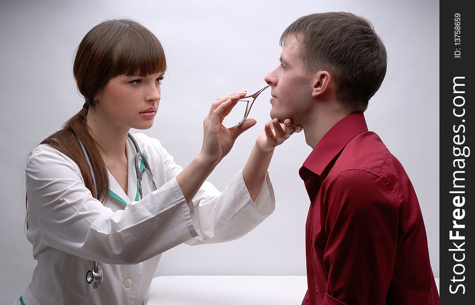 Young doctor inspecting patient's nose. Young doctor inspecting patient's nose