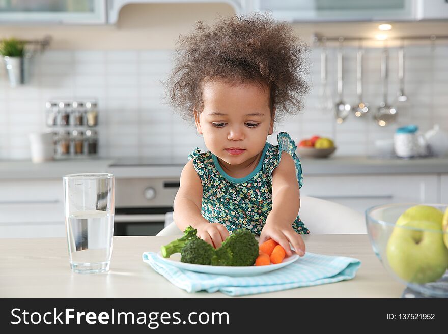 Cute African-American Girl Eating Vegetables At Table