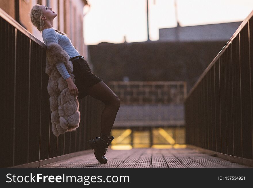 Photo side of blonde in fur vest on walk on bridge, blurred background