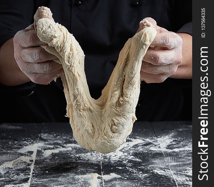 Cook stretches kneaded dough from white wheat flour over a black wooden table