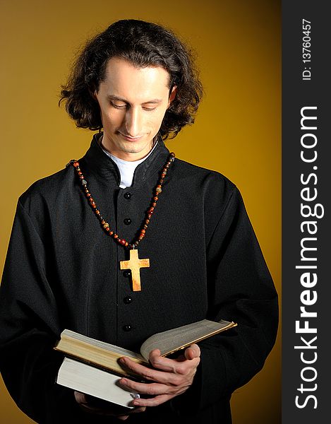 Conceptual portrait of Praying priest with wooden cross reading Holy Bible. yellow background