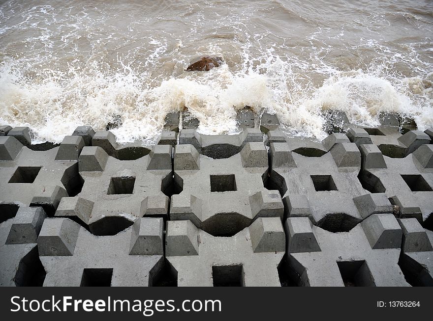 Breakwater with concrete blocks and wave at seaside