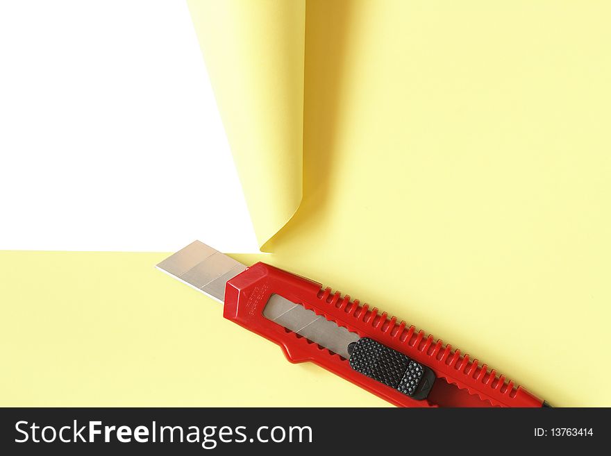 Red office knife cutting yellow paper sheet. Isolated on white with clipping path. Red office knife cutting yellow paper sheet. Isolated on white with clipping path