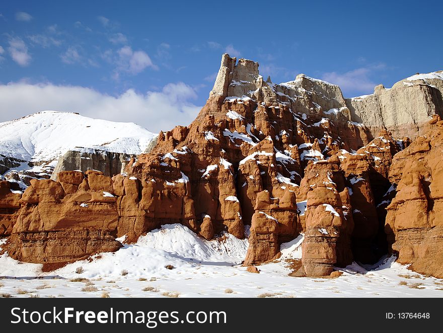 View of the red rock formations in Goblin Valley State Park with blue skyï¿½s and clouds and snow on the ground