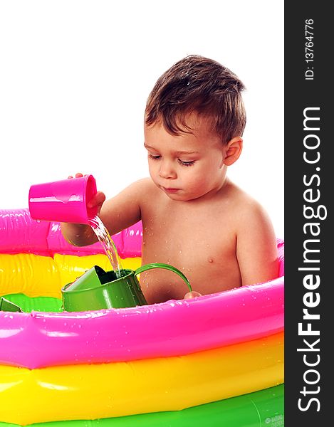 A toddler pouring water from one container into another while sitting in a brighly colored kiddie pool. Isolated on white.