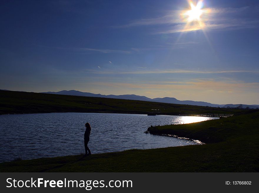 A girl walked to the edge of a quiet lake in the afternoon sunshine with blue sky. A girl walked to the edge of a quiet lake in the afternoon sunshine with blue sky