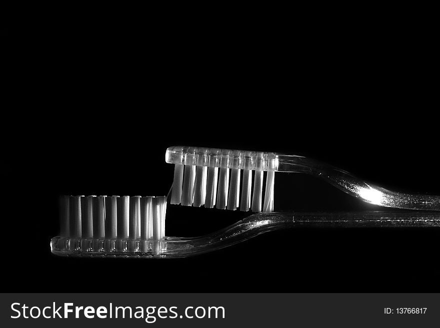 Two transparent toothbruses one over another in a intresting position on a black background. Two transparent toothbruses one over another in a intresting position on a black background