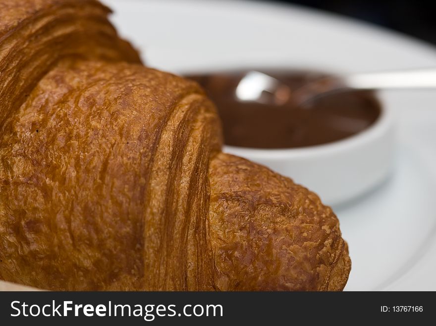 Croissant and chocolate sauce in the bowl with a spoon