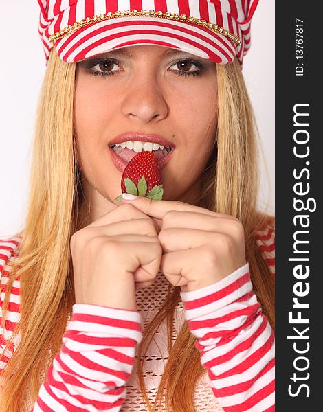 Beautiful young blonde woman eating strawberry, wearing hat with red and white stripes, shallow depth of field. Beautiful young blonde woman eating strawberry, wearing hat with red and white stripes, shallow depth of field