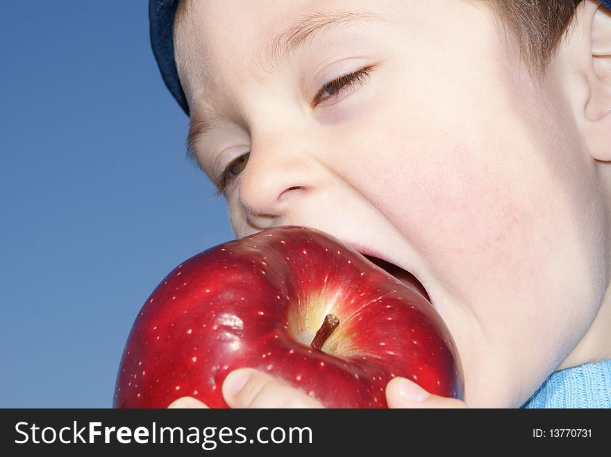 The child eagerly bites big red apple, the background sky. The child eagerly bites big red apple, the background sky