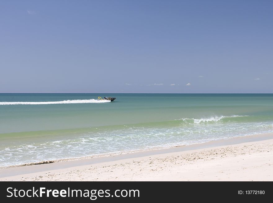 A speed motor boat cruising in the sea. White sand beach, turquoise ocean and blue sky.