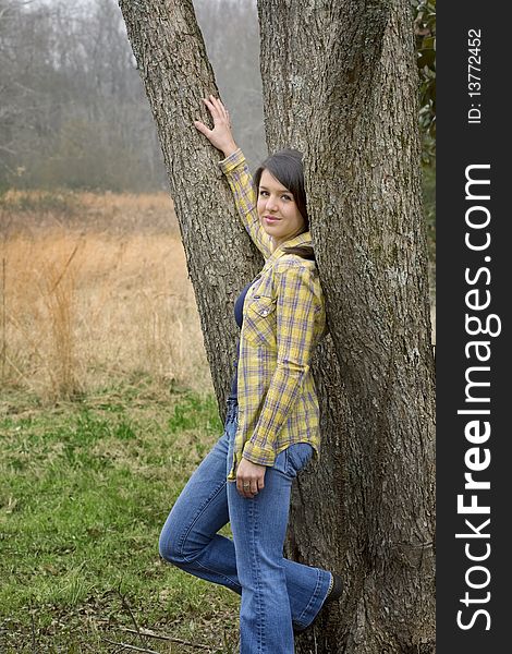 Young woman in yellow shirt and jean leaning against tree in pasture. Young woman in yellow shirt and jean leaning against tree in pasture