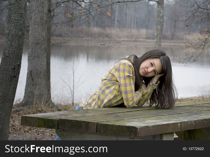Beautiful brunette woman in front of lake propped on picnic table. Beautiful brunette woman in front of lake propped on picnic table