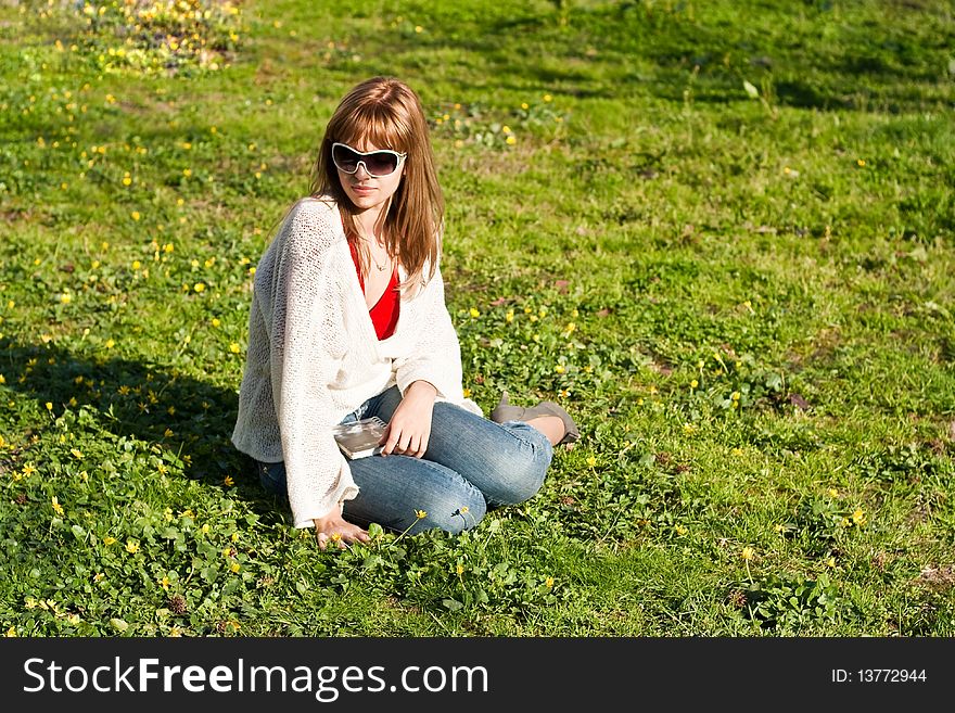 A girl in white woman's jacket sits on a green grass. A book on knees. A girl in white woman's jacket sits on a green grass. A book on knees.