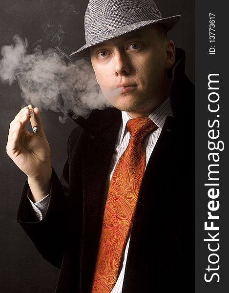 Handsome businessman with hat, coat and red tie. Serious face expression, smoking cigar. Handsome businessman with hat, coat and red tie. Serious face expression, smoking cigar.