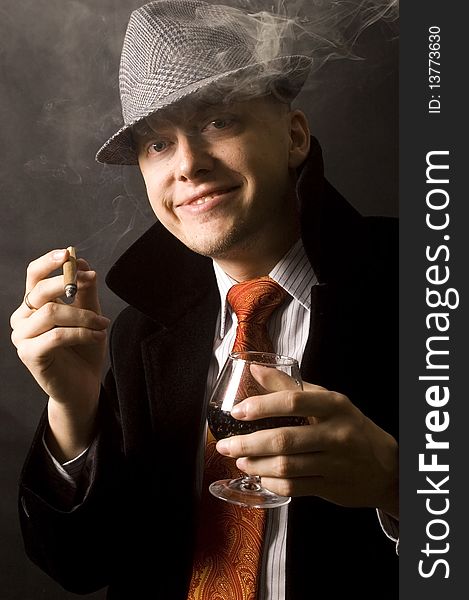 Elegant, handsome, young businessman. Wearing hat, necktie and black coat, holding cigar and drink. Elegant, handsome, young businessman. Wearing hat, necktie and black coat, holding cigar and drink.