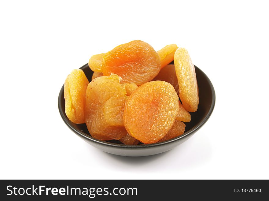 Dried juicy orange apricots in a small black bowl on a reflective white background. Dried juicy orange apricots in a small black bowl on a reflective white background