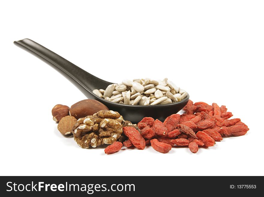 Sunflower seeds on a black spoon with mixed nuts and goji berries on a reflective white background. Sunflower seeds on a black spoon with mixed nuts and goji berries on a reflective white background