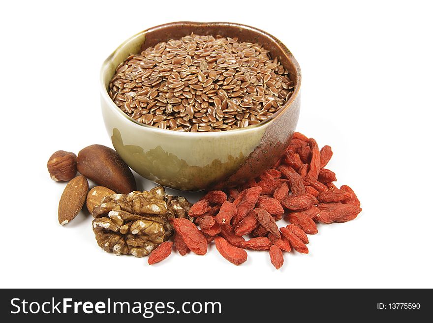 Bown linseed seeds in a small brown and green bowl with mixed nuts and goji berries on a reflective white background. Bown linseed seeds in a small brown and green bowl with mixed nuts and goji berries on a reflective white background