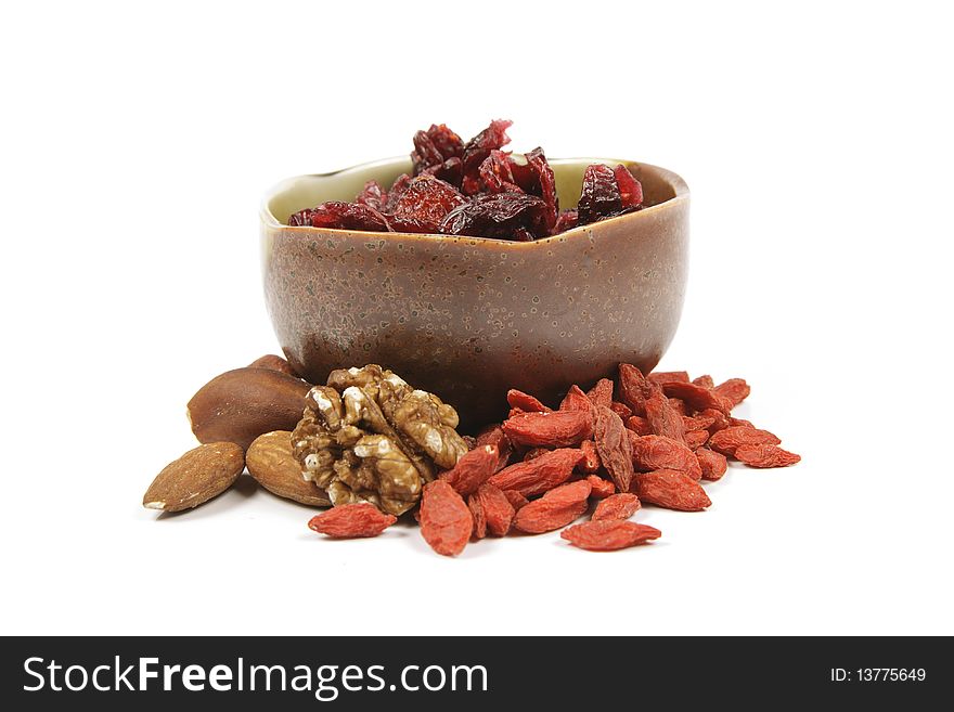 Red ripe dried cranberries in a small green and brown bowl with mixed nuts and goji berries on a reflective white background. Red ripe dried cranberries in a small green and brown bowl with mixed nuts and goji berries on a reflective white background