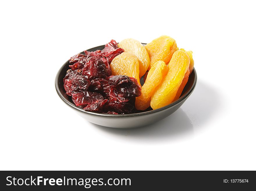 Red ripe dried cranberries and dried apricots in a small black bowl on a reflective white background. Red ripe dried cranberries and dried apricots in a small black bowl on a reflective white background