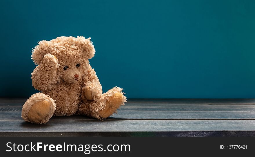 Teddy bear sad, sitting on the wooden floor, blue empty room background, copy space