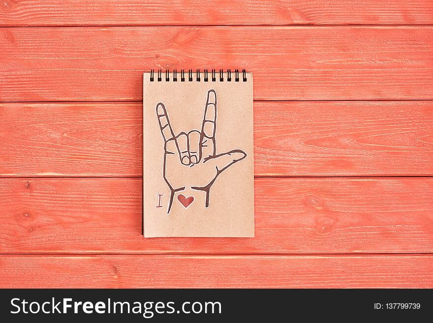 Notebook of Kraft paper with a painted symbol ASL American Sign Language ILY I Love you that lies on the textured wooden plank