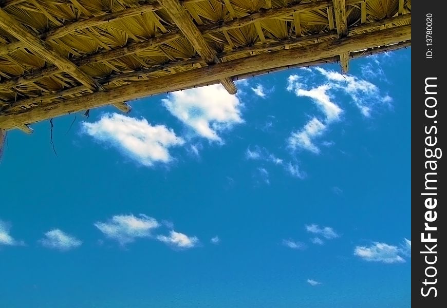 Blue sky with just a few puffy white clouds under a hut roof. Blue sky with just a few puffy white clouds under a hut roof