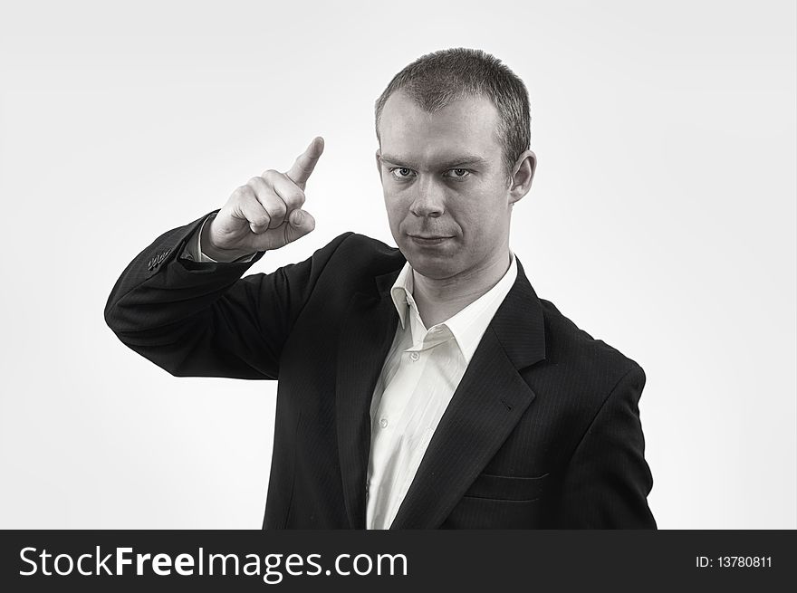 Young businessman in suit in angry pose, showing a point, on gray background