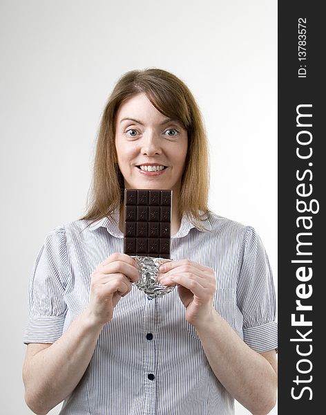 A vertical image of a pretty young woman smiling with a large bar of chocolate in her hand preparing to enjoy her treat. A vertical image of a pretty young woman smiling with a large bar of chocolate in her hand preparing to enjoy her treat