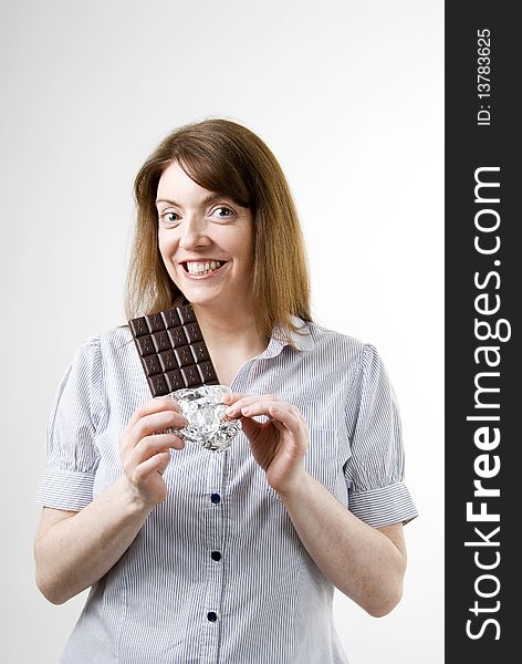 A vertical image of a pretty young woman happy and smiling in anticipation of the delicious chocolate bar she is holding and about to eat