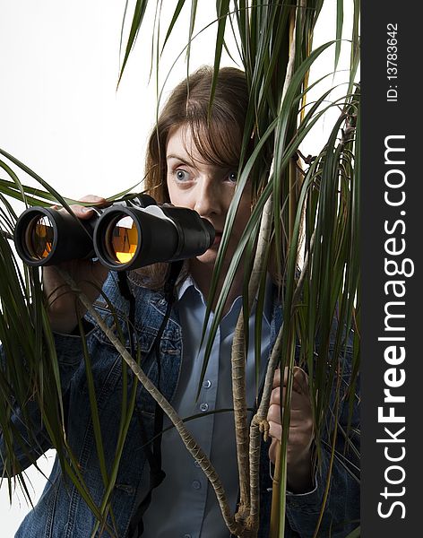 a vertical image of a young female with binoculars in hand hiding behind a bush and spying. a vertical image of a young female with binoculars in hand hiding behind a bush and spying