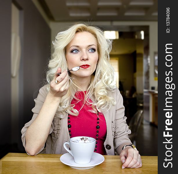 Young blonde in cafe at little table with cup of coffee. Young blonde in cafe at little table with cup of coffee