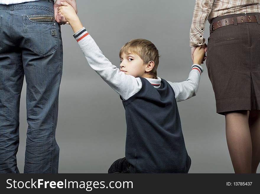 Young caucasian teenager boy together with parents looking back with anxious facial expression holding hands of parents isolated over gray background. Young caucasian teenager boy together with parents looking back with anxious facial expression holding hands of parents isolated over gray background