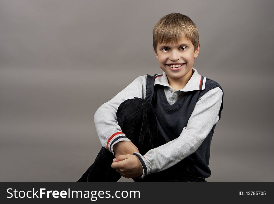 Cute and happy teenager boy with positive facial expression sitting and laughing isolated over gray background. Cute and happy teenager boy with positive facial expression sitting and laughing isolated over gray background