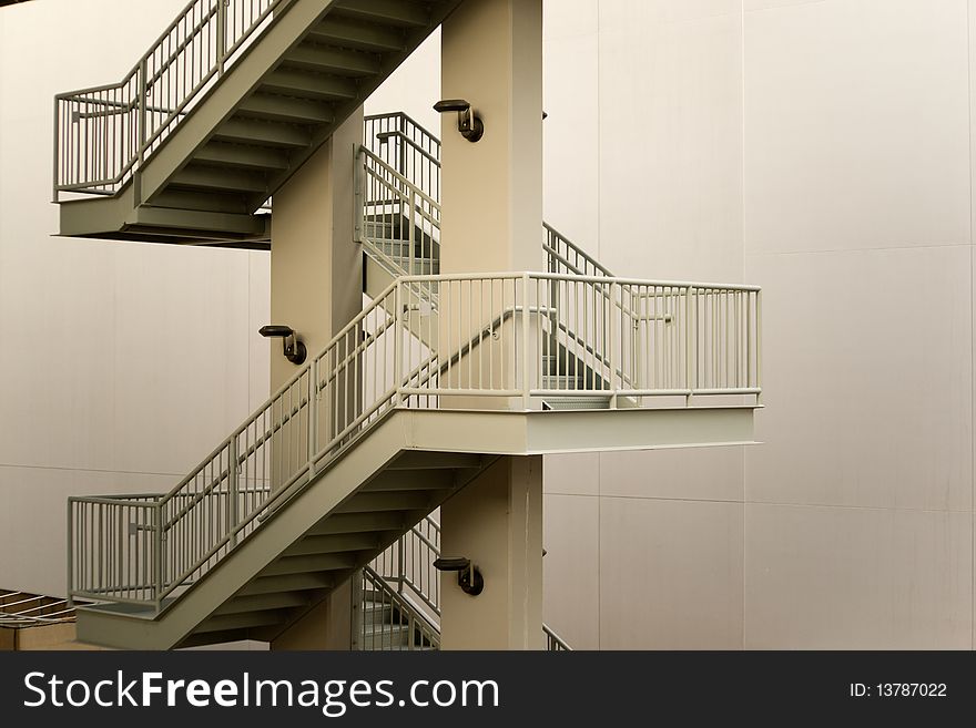 Perspective view of a zig-zag pattern of an exterior steel stairway against an empty wall. Perspective view of a zig-zag pattern of an exterior steel stairway against an empty wall