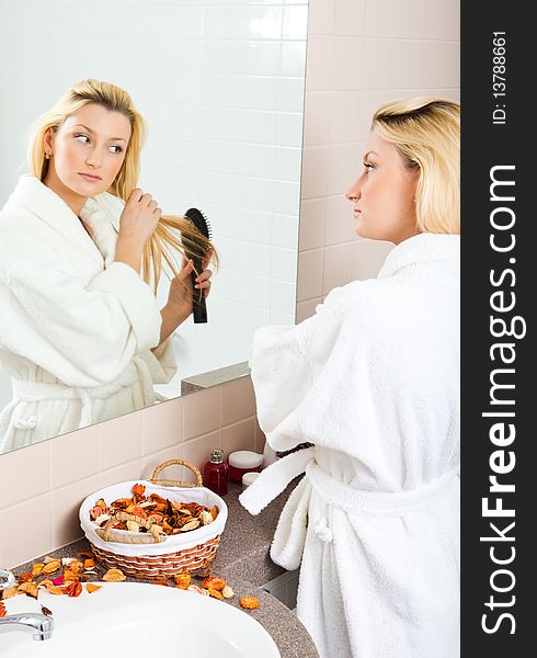 A young woman brushing hair in front of a bathroom mirror. Vertical shot.