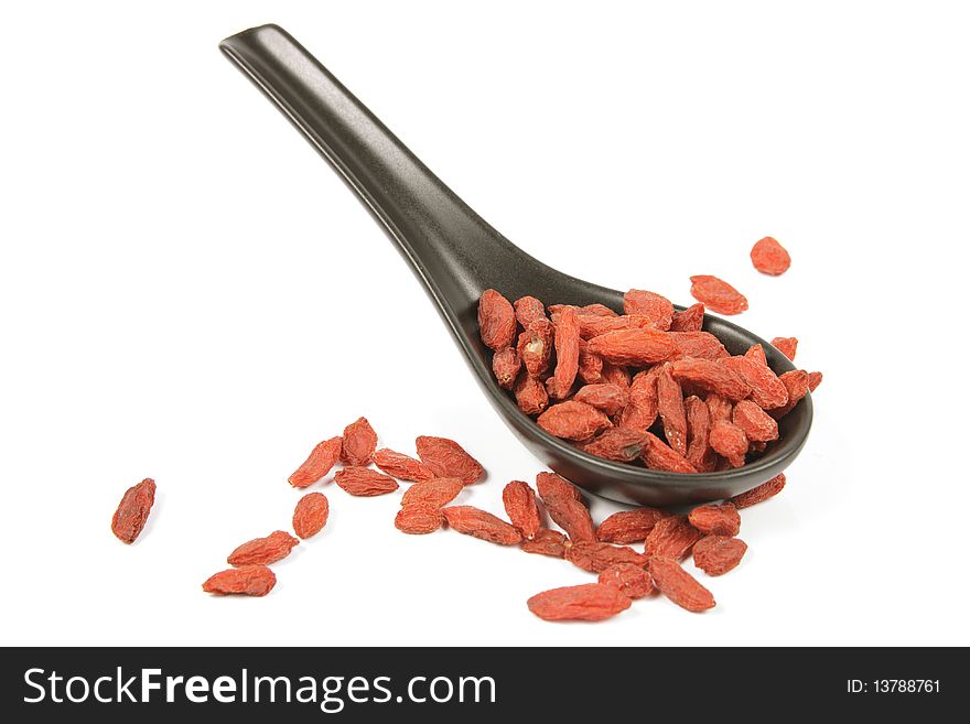 Red dry goji berries on a black spoon with a reflective white background