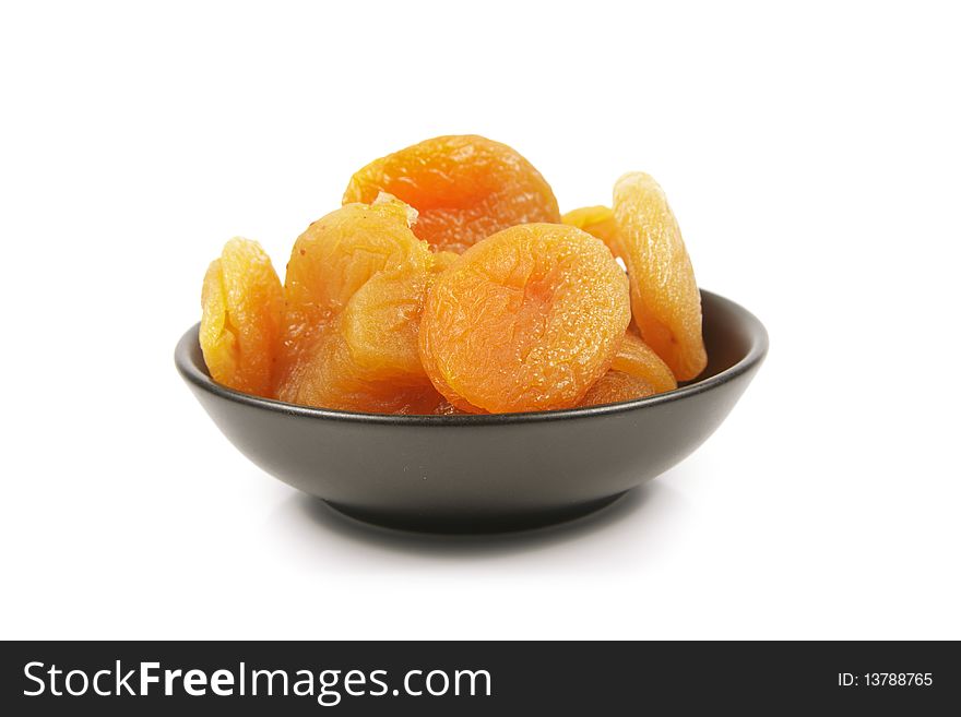 Dried juicy orange apricots in a small black bowl on a reflective white background. Dried juicy orange apricots in a small black bowl on a reflective white background