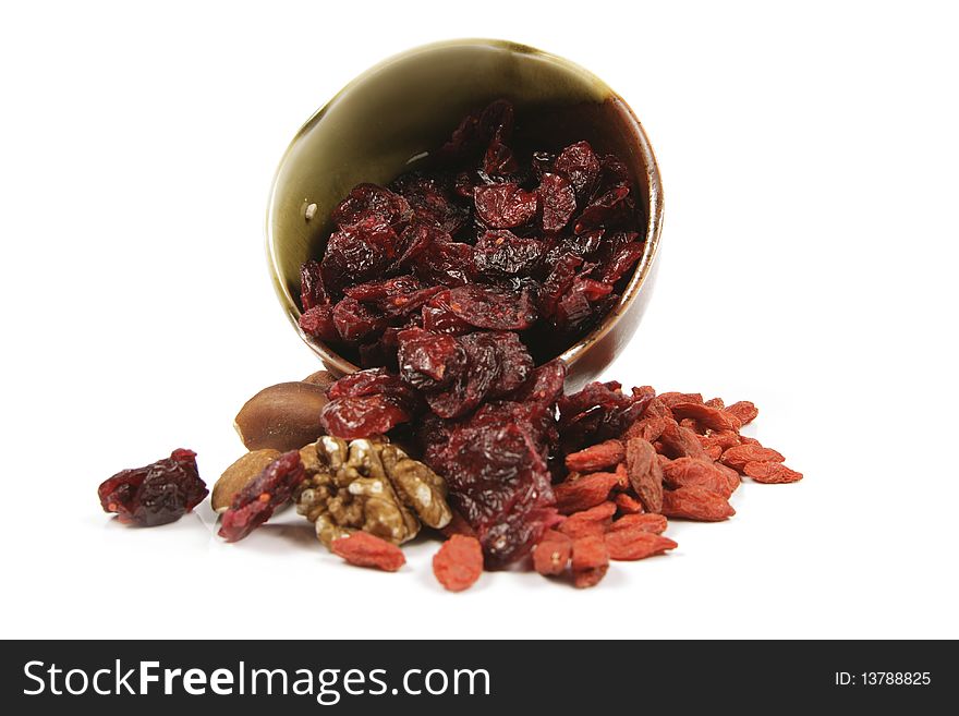 Red ripe dried cranberries spilling from a small bowl with mixed nuts and goji berries on a reflective white background. Red ripe dried cranberries spilling from a small bowl with mixed nuts and goji berries on a reflective white background