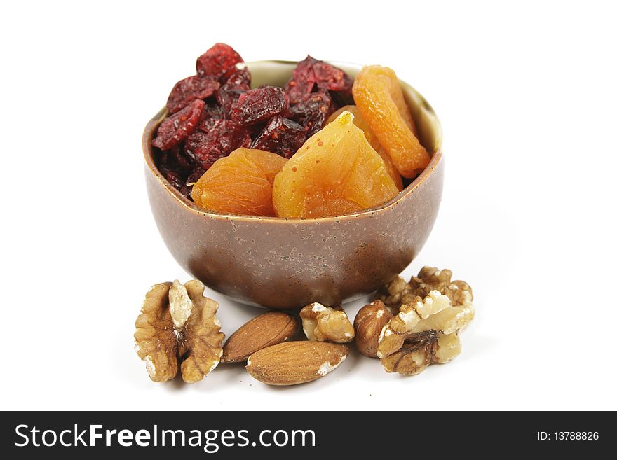 Red ripe dried cranberries and dried orange apricots in a small bowl with mixed nuts on a reflective white background. Red ripe dried cranberries and dried orange apricots in a small bowl with mixed nuts on a reflective white background